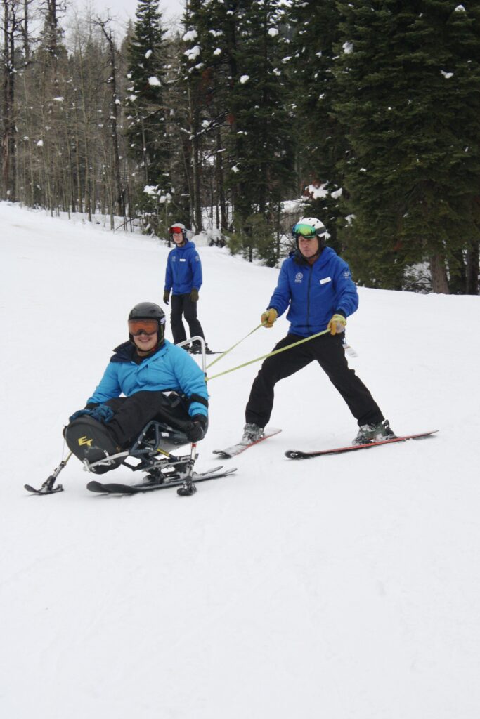 Fernando skiing on a bi-ski while being tethered by his instructor, Dave