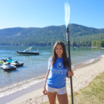 Achieve Tahoe volunteer, Audrey poses in front of Donner Lake while volunteering at Sierra Summer Sports.