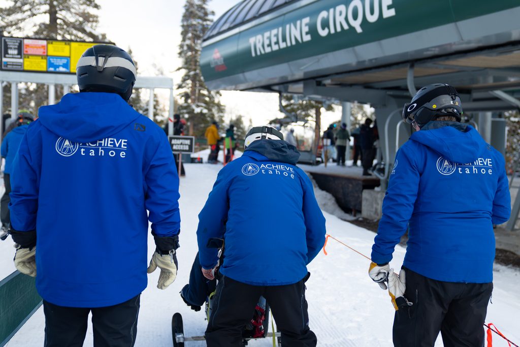 Achieve Tahoe volunteers push a participant towards the chairlift at Alpine